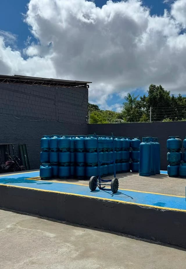 Pátio real da LÁGÁS com estoque de botijões azuis e carrinho de movimentação.